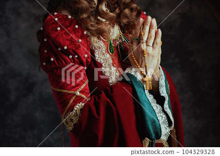 Closeup on medieval queen in red dress with rosary praying 104329328