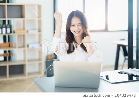 Portrait of a woman business owner showing a happy smiling face as he has successfully invested her business using computers and financial budget documents at work. Portrait of a woman business owner showing a happy smiling face as he has successfully invested her business using computers and financial budget documents at work. 104329478