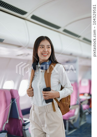 Young asian attractive woman travel by airplane, Passenger wearing headphone putting hand baggage in lockers above seats of plane. 104329581
