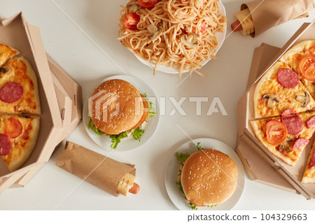 Top view image of pizza with mushrooms, cheese and meat, spaghetti with tomatoes, hamburger with fries, sausage in dough. Tasty and delicious dinner with junk food. 104329663