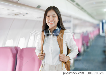Young asian attractive woman travel by airplane, Passenger wearing headphone putting hand baggage in lockers above seats of plane. 104330128