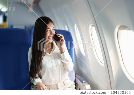 Asian business woman passenger sitting on business class luxury plane while working using smart phone mobile talking or video conference and travel concept. 104330163