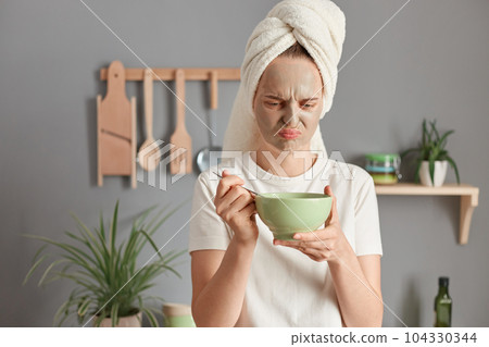 Horizontal shot of sad upset disappointed woman doing skin care procedures while having breakfast she doesn't like, looking in plate with disgusting expression. 104330344