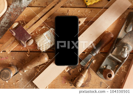 Big variety of equipments on wooden table, lot of tools on table, smart phone with blank screen in carpentry workshop, copy space for advertisement or promotional text. Big variety of equipments on wooden table, lot of tools on table, smart phone with blank screen in carpentry workshop, copy space for advertisement or promotional text. 104330501