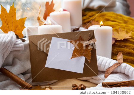 Empty paper note copy envelope space for your text on background of aesthetic atmosphere Autumn leaves spices and candle on knitted white sweater in warm yellow lights. Still life. Raining 104330962