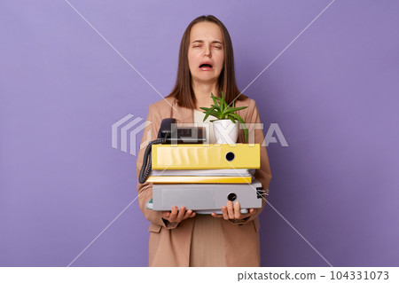 Portrait of depressed stressed Caucasian woman wearing official style jacket holding folders isolated over purple background, female lost her job, crying with despair. 104331073