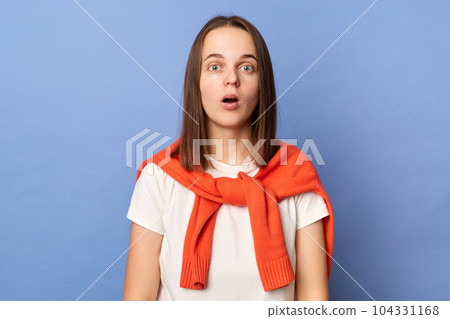 Photo of shocked amazed astonished, woman dressed white T-shirt and tied sweater over shoulders standing isolated on blue background, sees something surprised, looking at camera with big eyes. Photo of shocked amazed astonished, woman dressed white T-shirt and tied sweater over shoulders standing isolated on blue background, sees something surprised, looking at camera with big eyes. 104331168