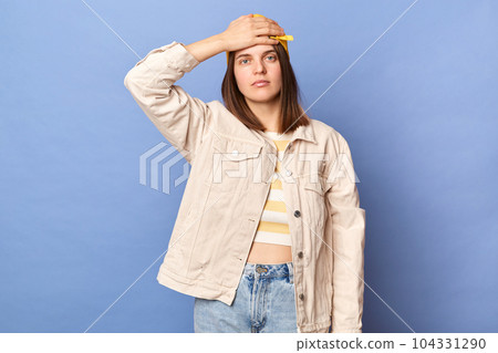 Indoor shot of despair dissatisfied teenager girl wearing baseball cap and jacket posing isolated over blue background, showing facepalm gesture, looking at camera with sad expression, loosing. 104331290