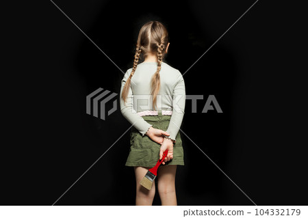 Child girl standing with her back and holding paint brush on blackboard background 104332179