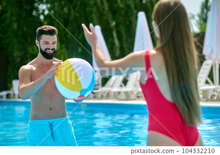 Happy attractive couple having fun in pool with beach ball. 104332210