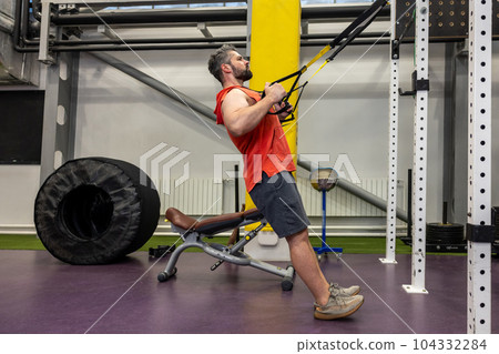 Athlete sporty man doing exercise with fitness trx straps to strengthen his muscle in gym. Athlete sporty man doing exercise with fitness trx straps to strengthen his muscle in gym. 104332284