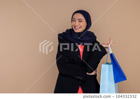 Cheerful Muslim woman in hijab standing with shopping bags Cheerful Muslim woman in hijab standing with shopping bags 104332332