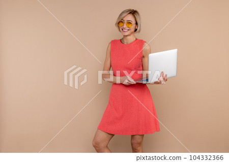 Happy woman in dress and sunglasses working online using laptop Happy woman in dress and sunglasses working online using laptop 104332366