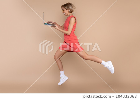Jumping woman in dress and sunglasses using laptop working online 104332368