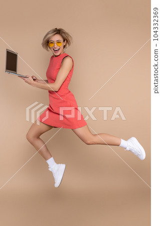 Jumping woman in dress and sunglasses using laptop working online Jumping woman in dress and sunglasses using laptop working online 104332369