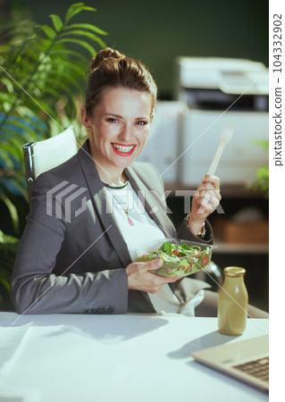 happy female employee in green office eating salad 104332902