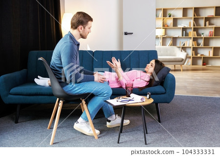 Attractive woman reclining comfortably on a couch talking to his psychiatrist explaining something Attractive woman reclining comfortably on a couch talking to his psychiatrist explaining something 104333331