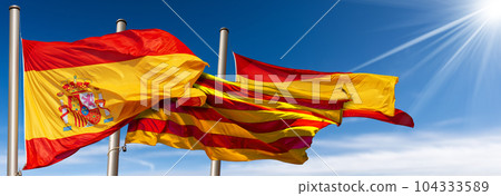Spanish and Catalan Flags Blowing in the Wind on Blue Sky with Clouds 104333589
