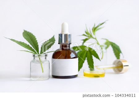 Dropper bottle with blank label near green cannabis leaves on white. CBD oil Mockup Dropper bottle with blank label near green cannabis leaves on white. CBD oil Mockup 104334011