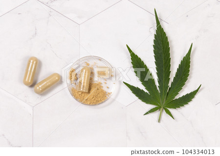 Capsules with hemp protein powder near green cannabis leaves. Alternative medicine 104334013