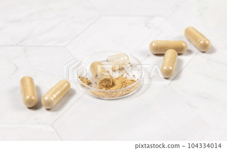 Taking dietary supplements with capsules. One capsule Opened in a jar on marble table Taking dietary supplements with capsules. One capsule Opened in a jar on marble table 104334014