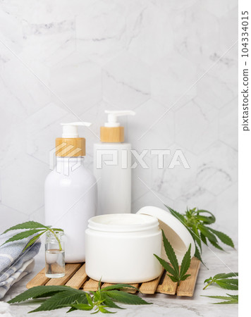 Opened cream jar with blank lid near green cannabis leaves close up, CBD cosmetic mockup 104334015
