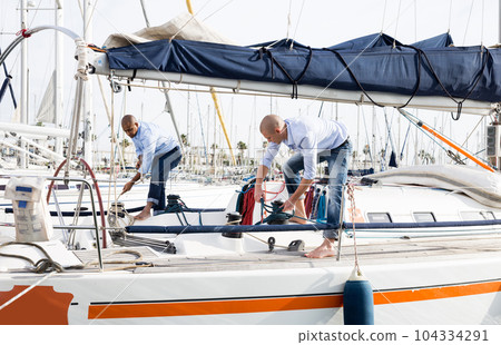 A couple of guys in blue shirts and jeans working on private sailing yacht in seaport 104334291