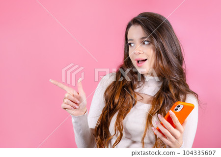 Happy young woman pointed by finger and standing isolated over pink background Happy young woman pointed by finger and standing isolated over pink background 104335607