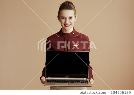 happy female air hostess on beige showing laptop blank screen 104336129