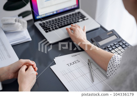 Woman accountant using a calculator and laptop computer while counting taxes for a client. Business audit and finance concepts Woman accountant using a calculator and laptop computer while counting taxes for a client. Business audit and finance concepts 104336179