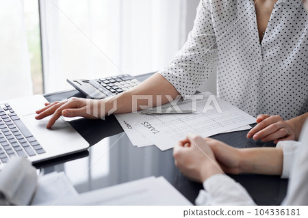 Woman accountant using a calculator and laptop computer while counting taxes for a client. Business audit and finance concepts 104336181
