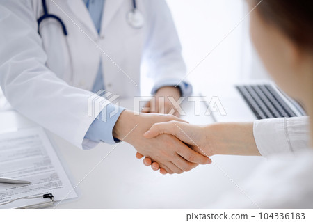 Doctor and patient shaking hands while sitting opposite of each other at the table in clinic, just hands close up. Medicine concept Doctor and patient shaking hands while sitting opposite of each other at the table in clinic, just hands close up. Medicine concept 104336183