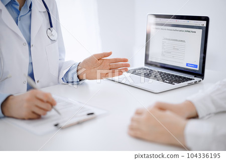 Doctor and patient sitting opposite each other at the desk in clinic. The focus is on female physician's hands pointing into laptop computer monitor, close up. Medicine concept Doctor and patient sitting opposite each other at the desk in clinic. The focus is on female physician's hands pointing into laptop computer monitor, close up. Medicine concept 104336195