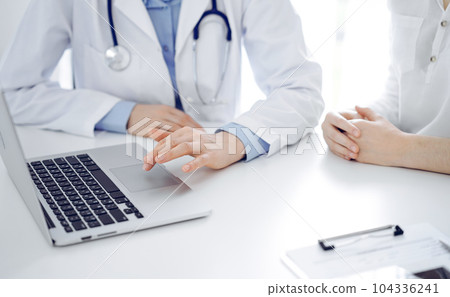 Doctor and patient sitting near each other at the desk in clinic. The focus is on female physician's hands using laptop computer, close up. Medicine concept Doctor and patient sitting near each other at the desk in clinic. The focus is on female physician's hands using laptop computer, close up. Medicine concept 104336241
