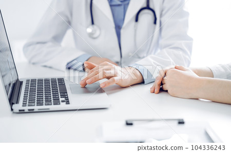 Doctor and patient sitting near each other at the desk in clinic. The focus is on female physician's hands using laptop computer, close up. Medicine concept Doctor and patient sitting near each other at the desk in clinic. The focus is on female physician's hands using laptop computer, close up. Medicine concept 104336243