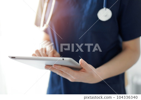Doctor woman using tablet computer while standing near panorama window in clinic, close up. Physician or surgeon at work. Medicine concept 104336340