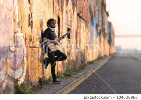 Romantic man hipster wearing sunglasses standing by the wall playing electric guitar at early sunset 104336966