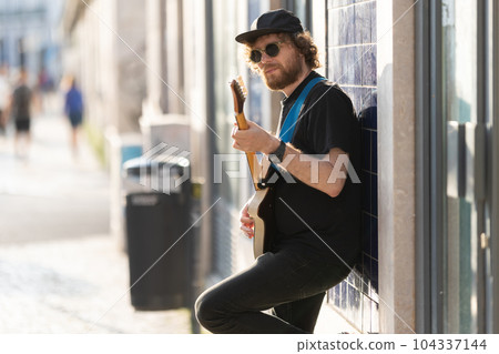 A man hipster wearing sunglasses standing by the wall and playing guitar 104337144