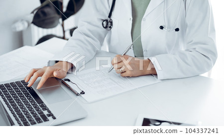 Unknown doctor woman sitting and writing notes at the desk in clinic or hospital office, close up. Medicine concept Unknown doctor woman sitting and writing notes at the desk in clinic or hospital office, close up. Medicine concept 104337241
