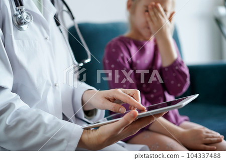 Doctor woman and kid patient at home. The pediatrician uses a tablet computer, close up. Medicine, healthcare concepts Doctor woman and kid patient at home. The pediatrician uses a tablet computer, close up. Medicine, healthcare concepts 104337488