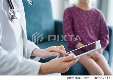 Doctor woman and kid patient at home. The pediatrician uses a tablet computer, close up. Medicine, healthcare concepts Doctor woman and kid patient at home. The pediatrician uses a tablet computer, close up. Medicine, healthcare concepts 104337513