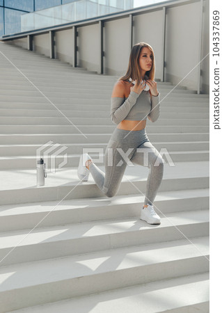 Sporty european woman stretching legs on stairs before running outdoors 104337869