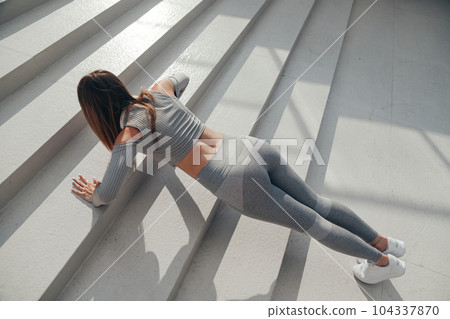 Young woman in grey clothes workout push -up in summer day in the city on stairs Young woman in grey clothes workout push -up in summer day in the city on stairs 104337870