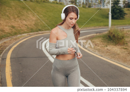 Beautiful woman with white headphones runs and listening to music in city. Beautiful woman with white headphones runs and listening to music in city. 104337894