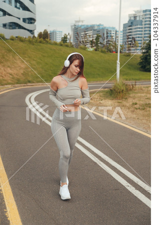 Beautiful woman with white headphones runs and listening to music in city. Beautiful woman with white headphones runs and listening to music in city. 104337914
