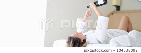Woman in bathrobe lying in white bed and pouring champagne into glass Woman in bathrobe lying in white bed and pouring champagne into glass 104338092