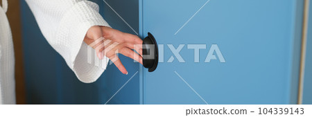 Woman in white bathrobe opening door of blue wardrobe in hotel with hand closeup 104339143