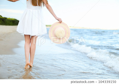 Young woman on a beach holding a white hat. Legs close up 104339150