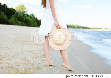 Young woman on a beach holding a white hat. Legs close up 104339152
