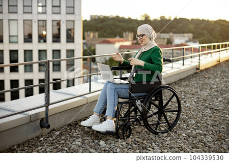 Muslim lady in wheelchair holding web conference via laptop Muslim lady in wheelchair holding web conference via laptop 104339530
